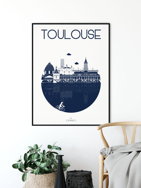 Affiche "Toulouse – La Ville" en marine, accrochée au mur, accompagnée d'une plante verte et d'une table basse.